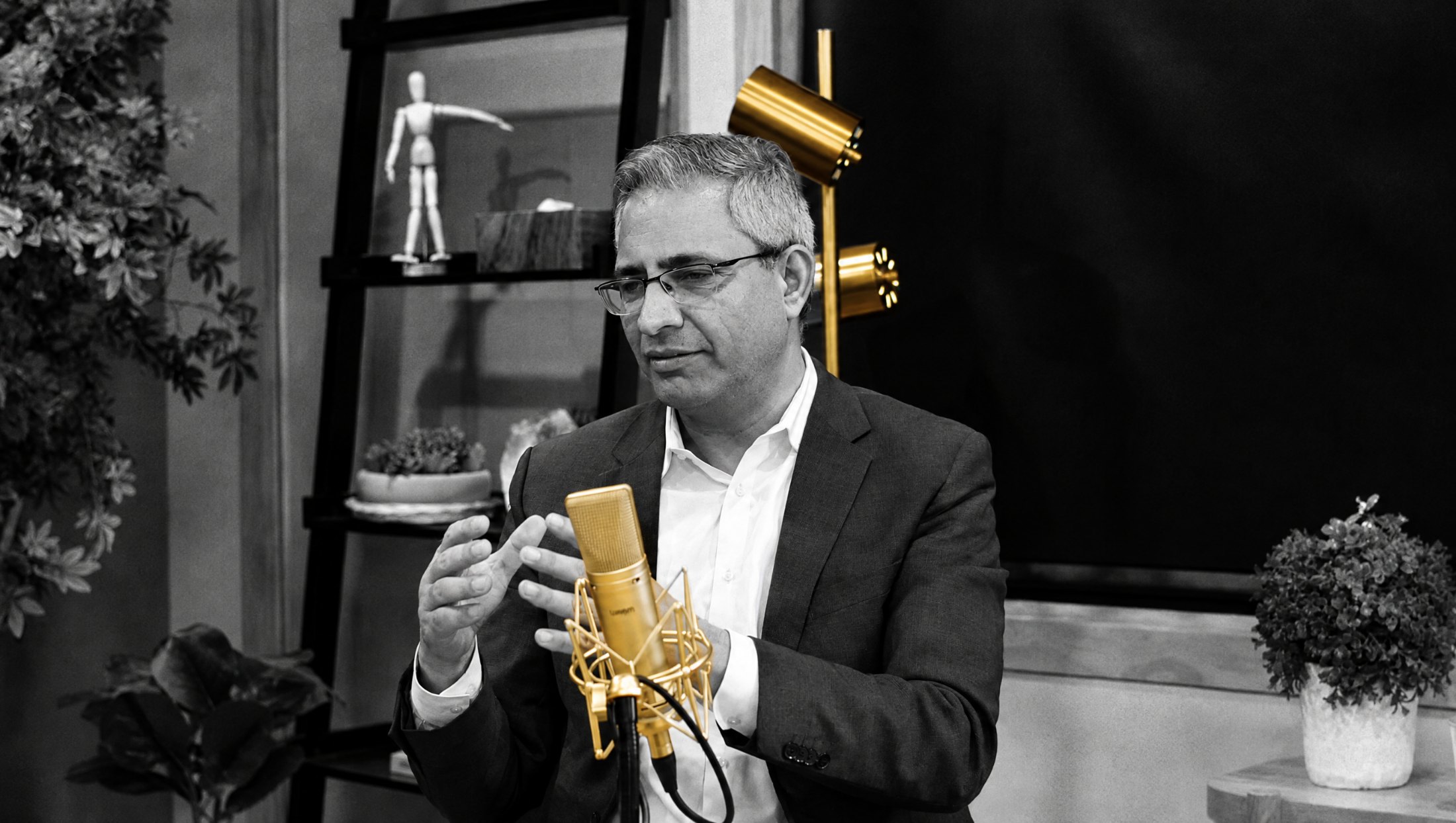 Dr. Sunil Wattal speaking with his hands, in black and white with the brass microphone and lamp glowing gold